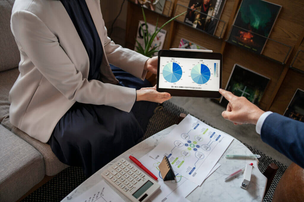 Two professionals analyzing customizable forecasting models on a tablet, displaying pie charts that represent unique revenue streams. The setting includes a business environment with financial documents, calculators, and pens on the table, indicating an in-depth financial planning session