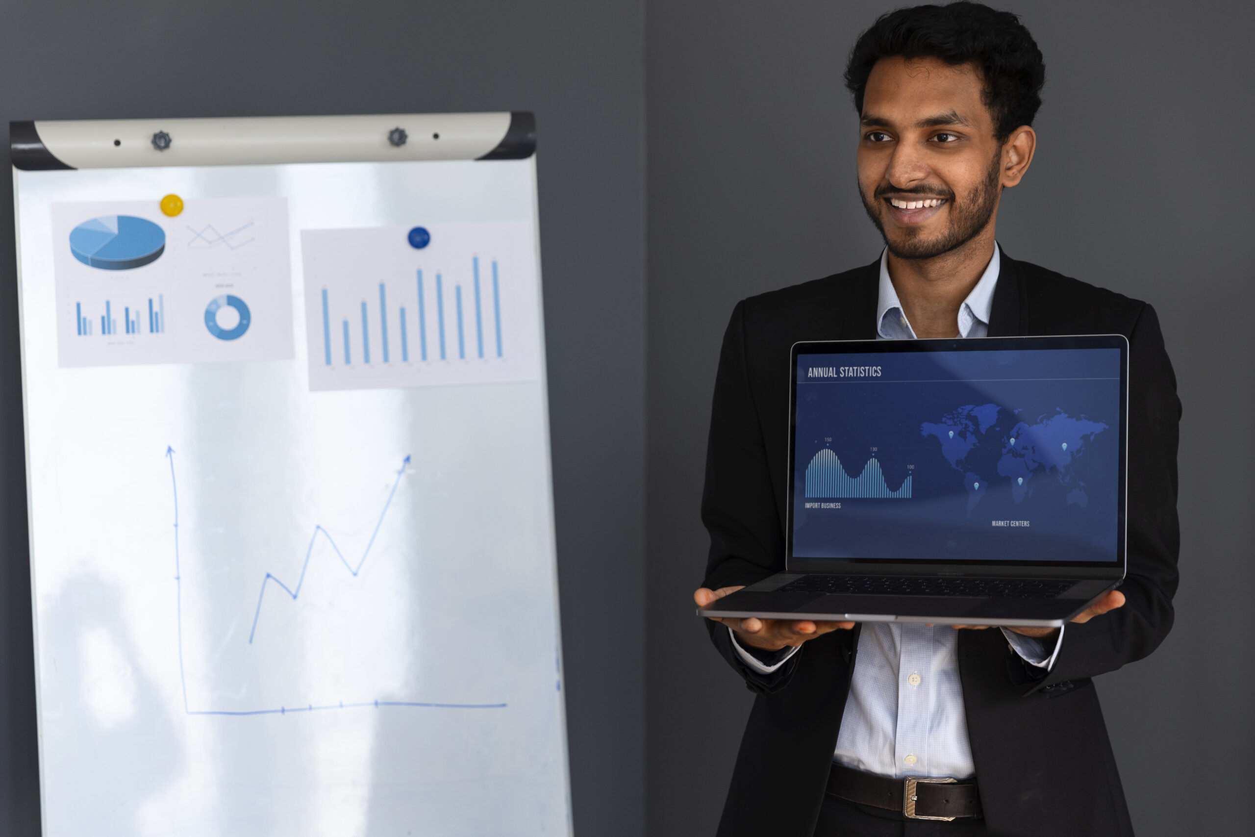 A professional individual standing in front of a presentation board, holding an open laptop that displays advanced revenue forecasting models. The board includes various financial data analysis charts, symbolizing the expertise of RSB Healthcare Consulting in healthcare finance and revenue cycle management