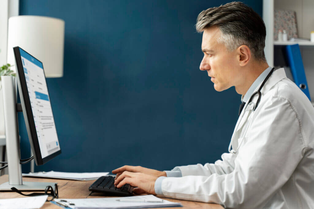 A healthcare professional in a white lab coat working on a computer, symbolizing the process of medical coding and charge entry, an essential administrative task in healthcare