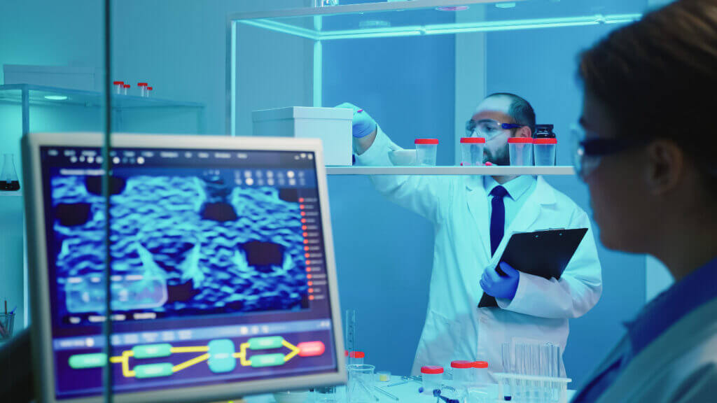 A healthcare professional evaluates laboratory samples while advanced analytics are displayed on a computer monitor, symbolizing the critical role of data analytics in enhancing revenue management and decision-making processes within healthcare organizations