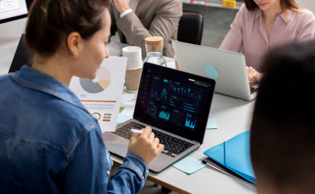 A visual representation of healthcare administrators analyzing financial data on a laptop, showcasing graphs and charts related to revenue cycle analytics components such as claim analysis, denial management, and patient scheduling. The image reflects a collaborative effort to enhance financial operations through advanced analytics techniques