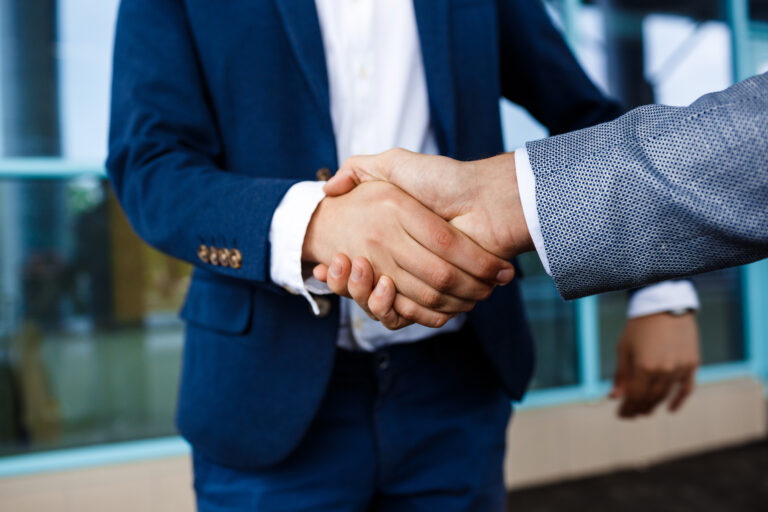 Professionals in a collaborative handshake in front of a modern office, symbolizing the partnership with RSB Healthcare Consulting for enhanced revenue cycle operations and financial sustainability in healthcare