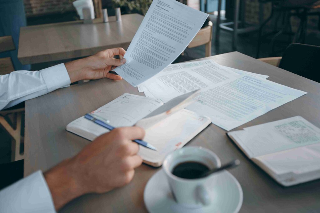 A professional setting with an individual reviewing documents for Provider Credentialing and Enrollment, with a pen in hand and a cup of coffee on the table.